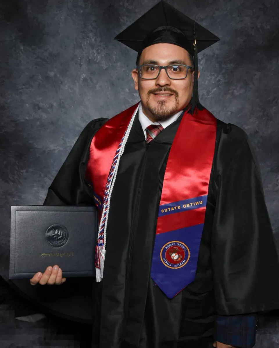 Business management graduate Jon Rodriguez posing in cap and gown holding diploma